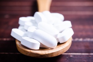 Close up white pills tablets on wooden spoon with wooden board background