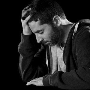 young desperate man suffering with hand on head in deep depression, pain , emotional disorder, grief and desperation concept isolated on black background with grunge studio lighting black and white