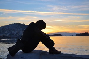 Person sitting on lake shore sad about Alcoholism