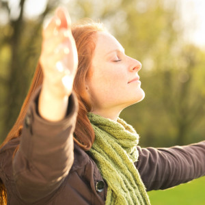 Woman worshiping with open arms or taking in the Autumn sun in a park.