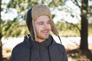 Smiling young man in warm clothing looks to his side in forest on a winter day