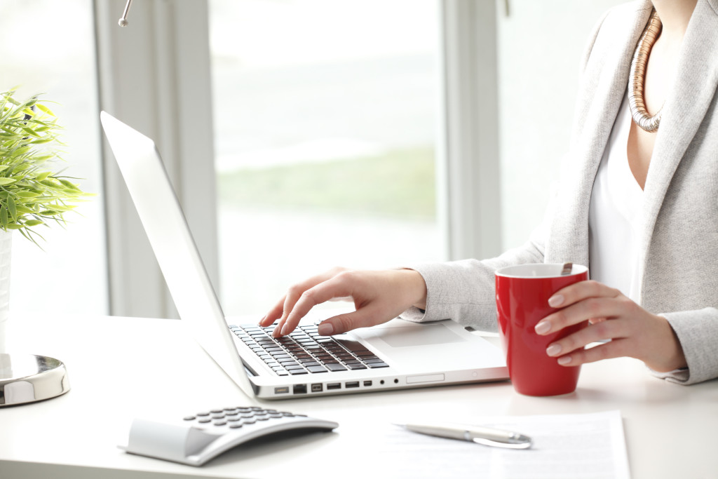 Close-up of businesswoman sitting at desk and typing on keyboard in office.