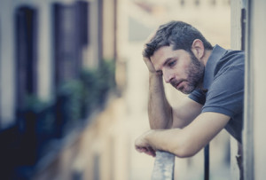 young man alone outside at house balcony terrace looking depressed, destroyed, wasted and sad suffering emotional crisis and depression on urban background