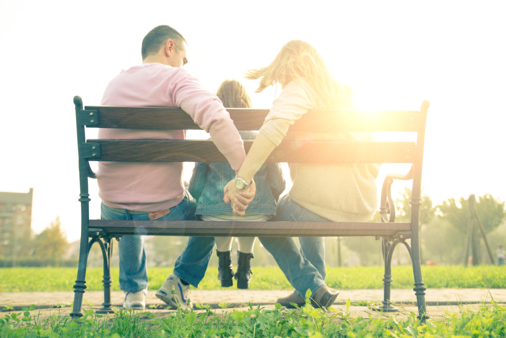 Family sitting on a bench - Mom and dad holding hands and daughter sitting in the middle