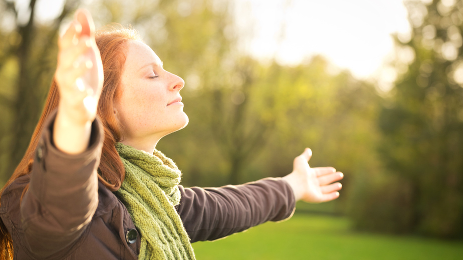 Woman worshiping with open arms or taking in the Autumn sun in a park.