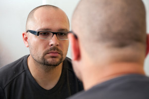 sad man in glasses looks in mirror