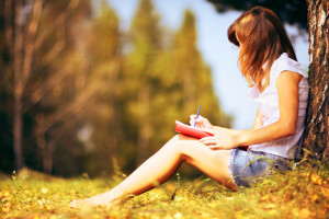 Young female student sitting near a tree and studying.