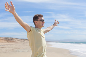 young smiling man standing at the beach with arms wide open, freedom or happiness concept