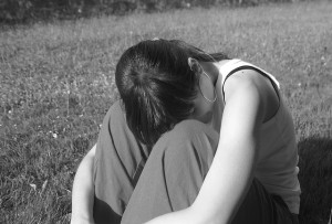 Girl sitting in grass with head between knees