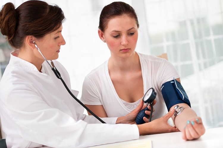 Female doctor checking young woman blood pressure