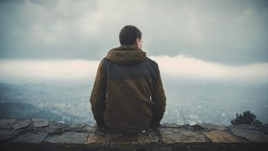 Young man sitting on rock wall over looking valley thinking about Dextromethorphan