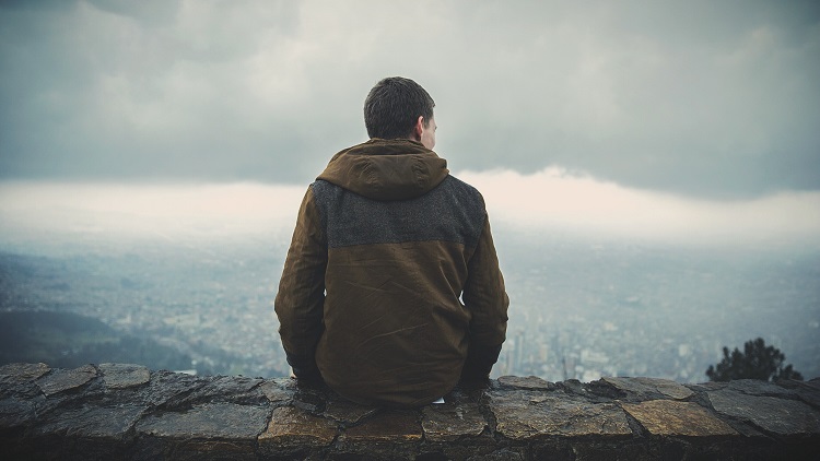 Young man sitting on rock wall over looking valley