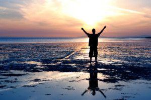 inspiring man silhouette on beach with arms raised in faith