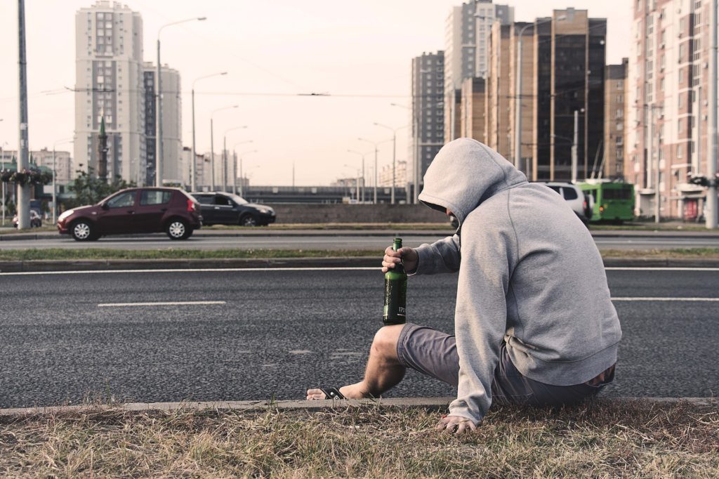 Man sitting on a curb with a beer in his hand