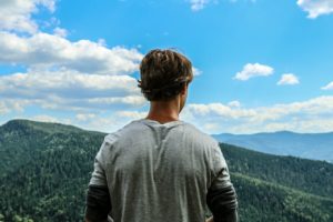 Young man looking at mountains thinking about Faith and Treatment for Substance Abuse